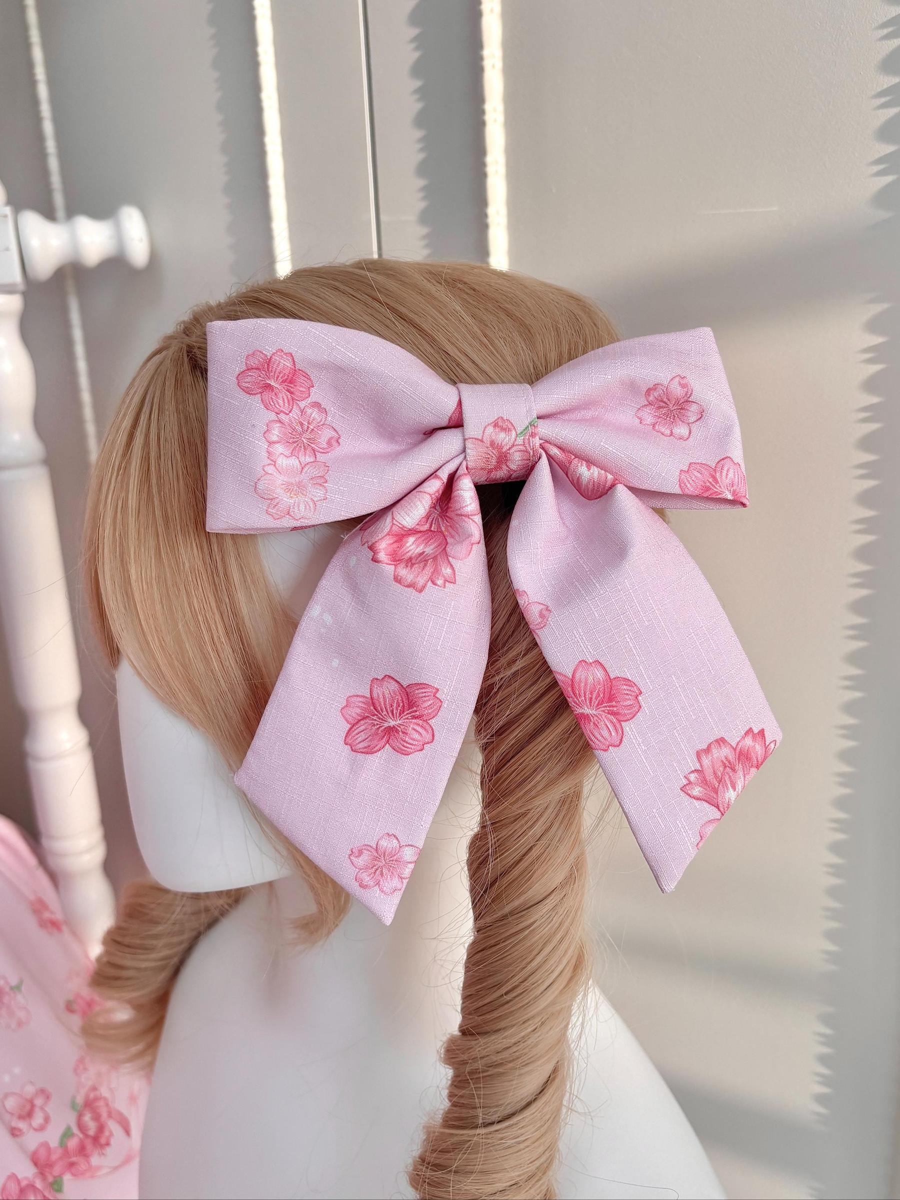 Close-up detailed view of oversized sakura bunny hair bow clip in pink fabric with cherry blossom floral print on mannequin with brown curly twin ponytails lolita hairstyle coordination