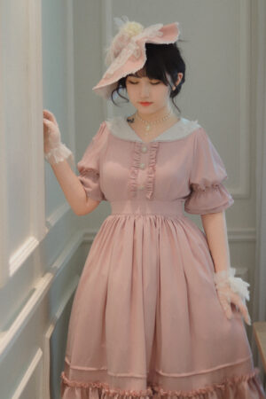 Plus size vintage lolita OP dress dusty pink color with white square collar puff sleeves and lace flounce front three-quarter view on female model with lace gloves and fancy hat in retro indoor corridor setting