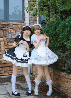 Cat cafe maid lolita one-piece dress front full-body view outdoor, blue-pink and black-white colorways, puffed sleeves, ruffled skirt, detachable apron with cat paw embroidery, maid headband accessory