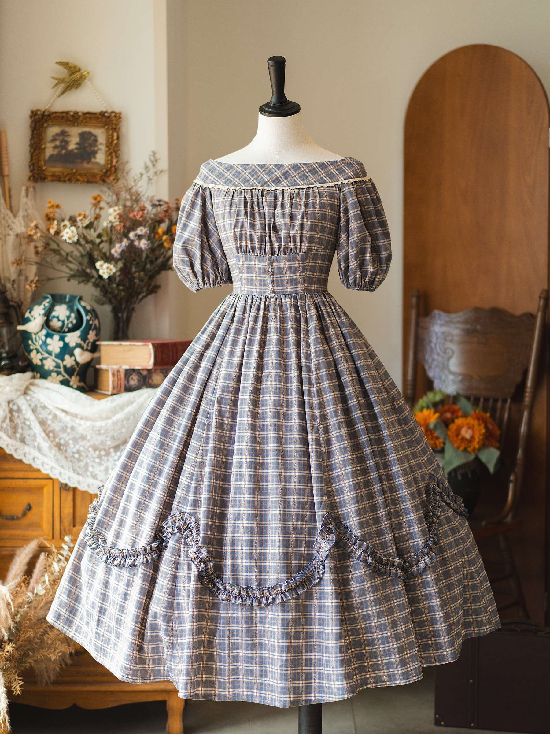 Blue-brown plaid Lolita OP dress with puff sleeves and ruched bust design on mannequin against vintage studio chair backdrop