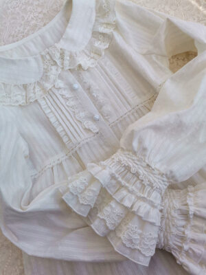 Close-up overhead view of delicate lace-ruffled peter pan collar with shirred layered lace cuffs and front button placket with lace trim details on white long-sleeve lolita cotton blouse