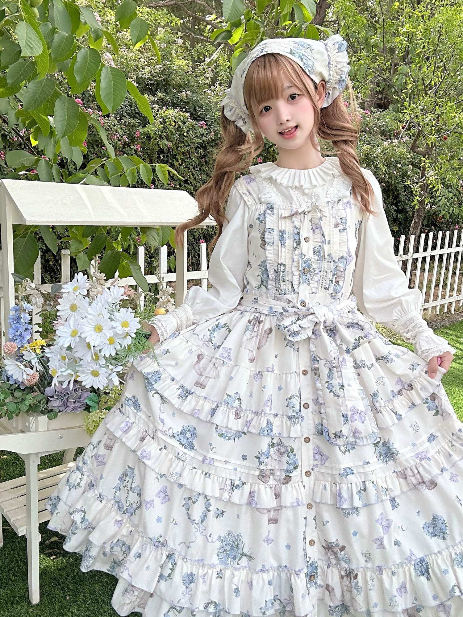 Meow Wreath Lolita JSK dress with matching inner blouse hair bonnet outdoor garden white fence floral ornaments full-body front view ruffled neckline waist bow multi-layered skirt