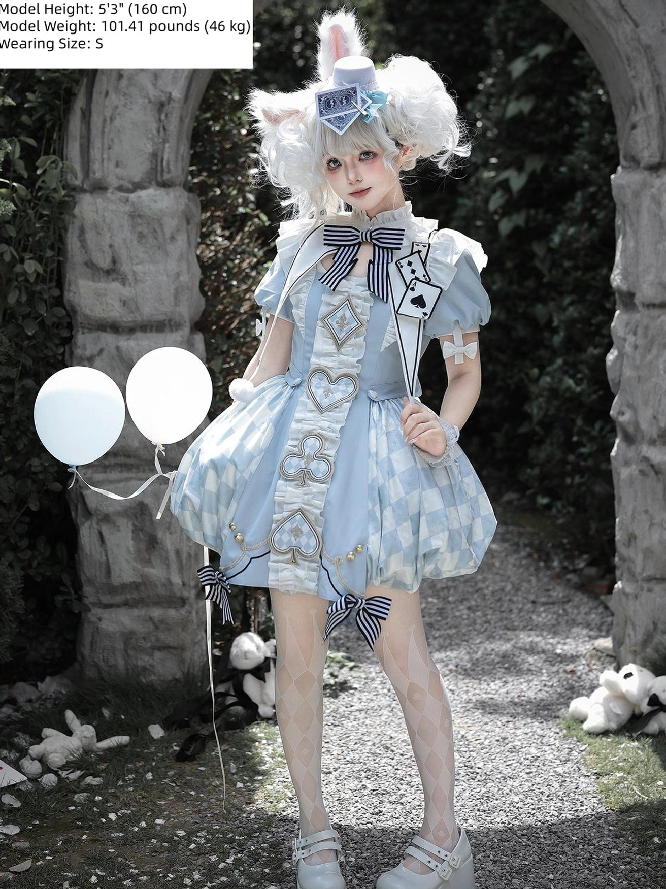 Model in blue Alice Lolita OP dress holding light blue balloons in stone arch garden, showing heart and playing card embroidery details, classic doll-like silhouette with bubble hem