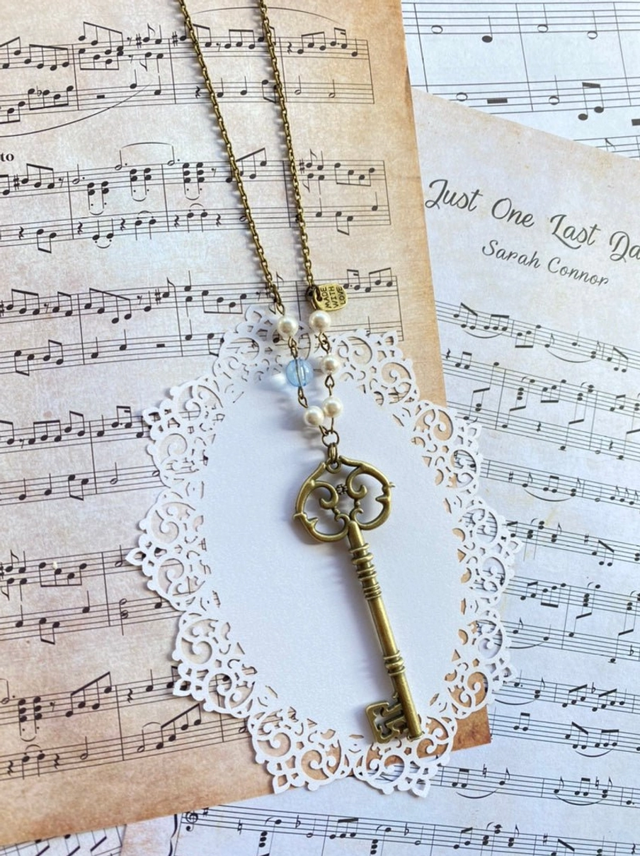 Antique key pendant Lolita sweater chain necklace with matching retro vintage aesthetic shown on sheet music and song note card styling background