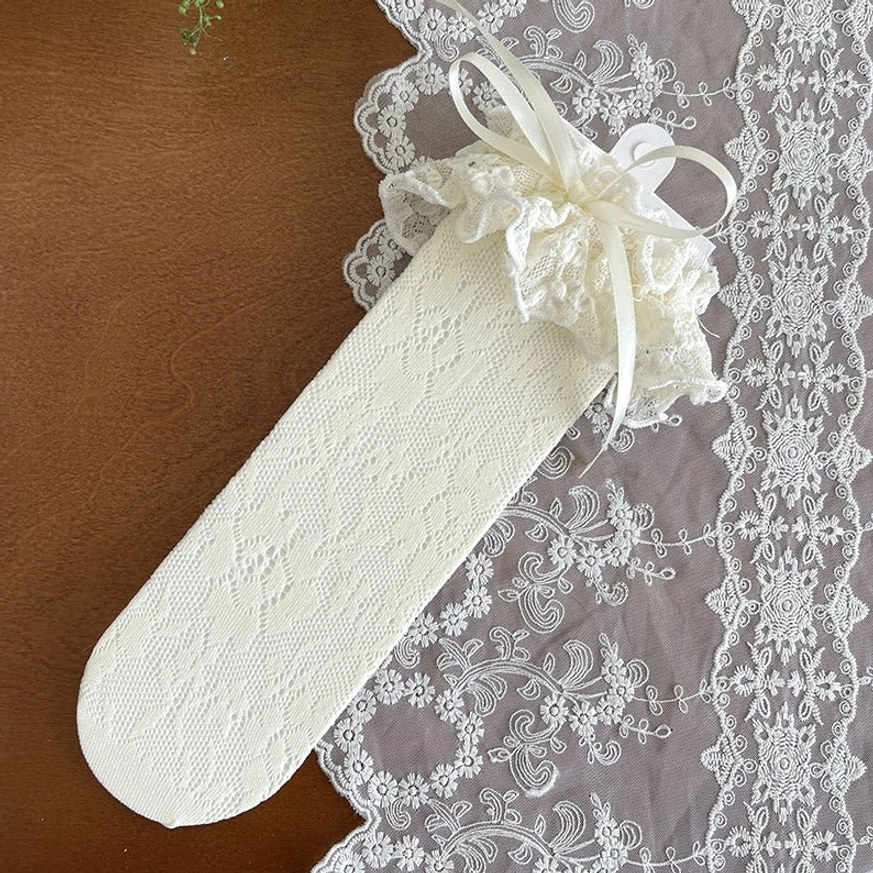 Single apricot French Lolita mid-calf lace sock close-up showing delicate floral lace texture, ruffled cuff and color-coordinated satin bow decoration on embroidered placemat