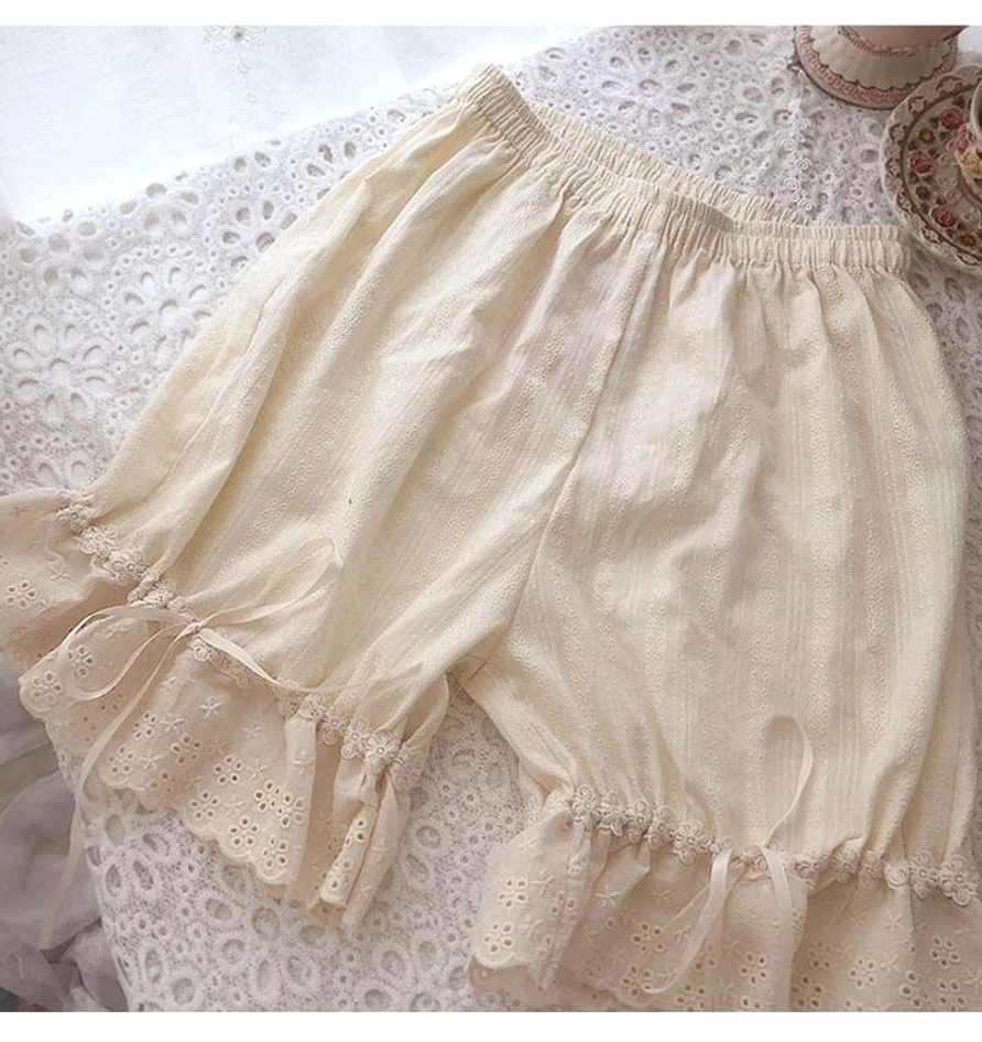 Apricot colored premium lolita cotton bloomers displayed on delicate lace tablecloth background featuring vertical jacquard embossed texture, intricately embroidered lace leg hem with scalloped edge, decorative side ribbon tie bows, and elasticated waistband construction detail