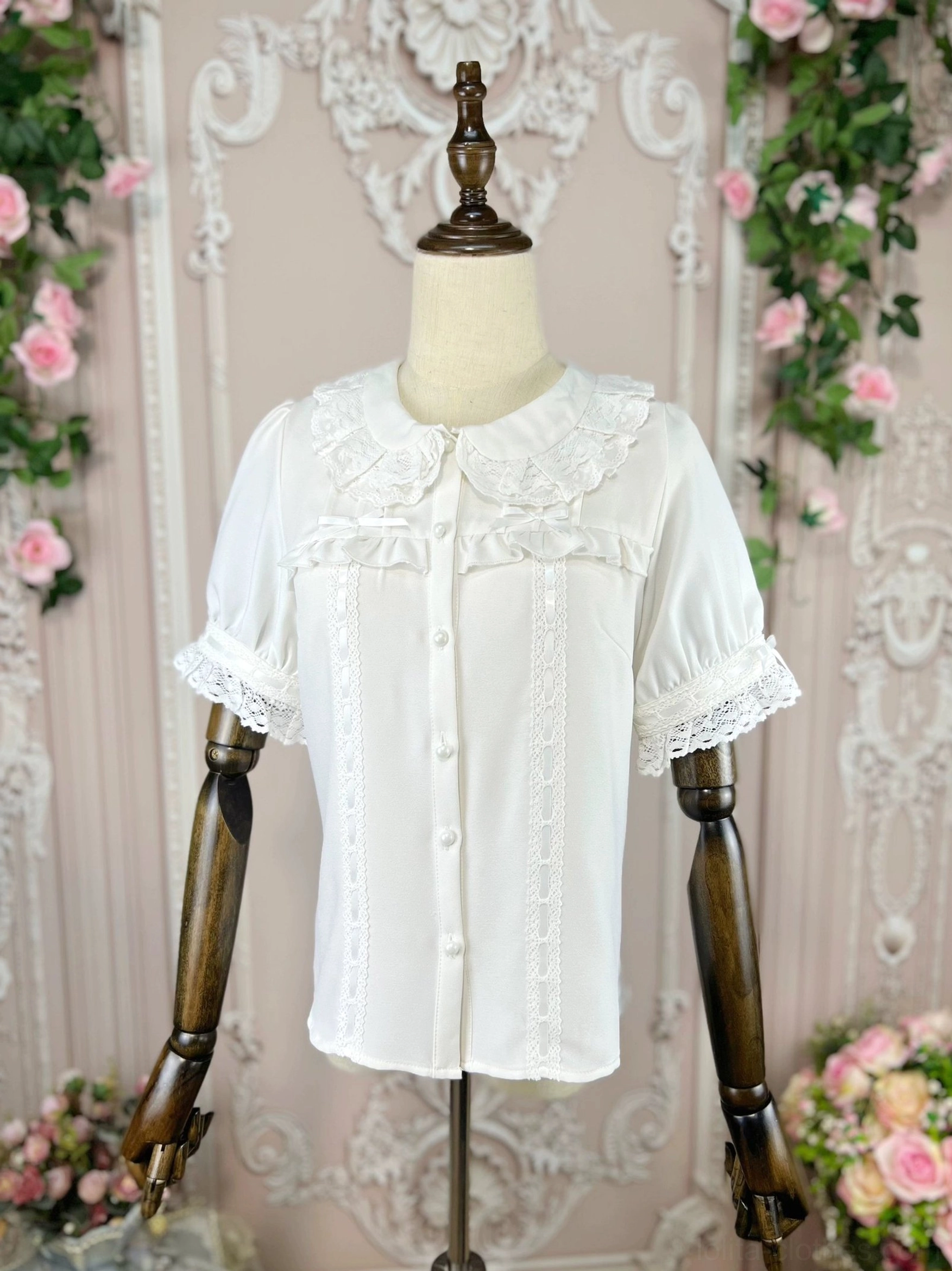 Apricot lolita doll collar blouse worn on wooden mannequin in front three-quarter view showing clear lace collar sleeve trims and full front button placket against vintage pink floral carved wall