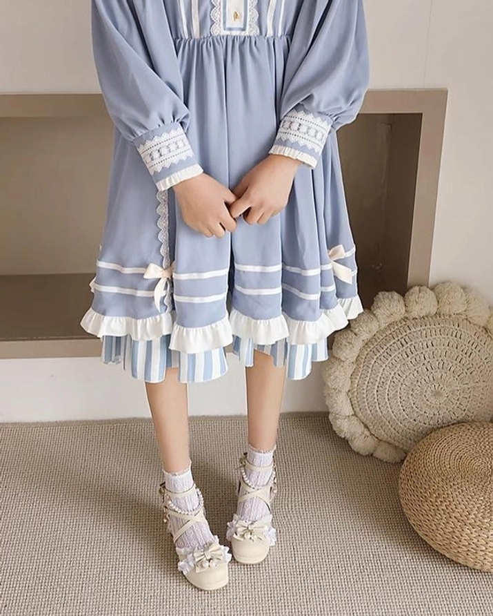 Front full standing view of apricot Lolita dress shoes with minimalist bow straps round toe low chunky heel worn with blue long-sleeve Lolita dress and ankle socks indoors