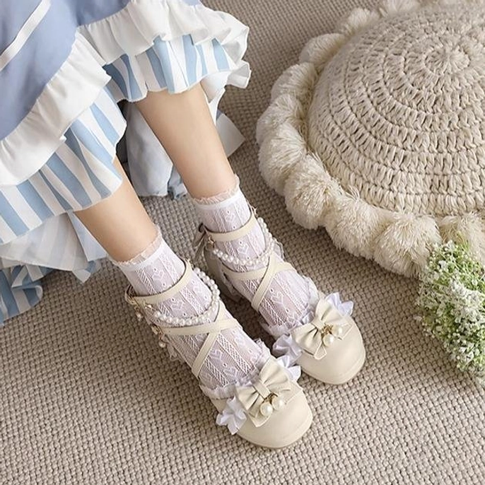 Overhead side view of apricot Lolita lace sandals with bowknot pearl decorations and cross lace straps low block heel paired with blue Lolita skirt on linen floor
