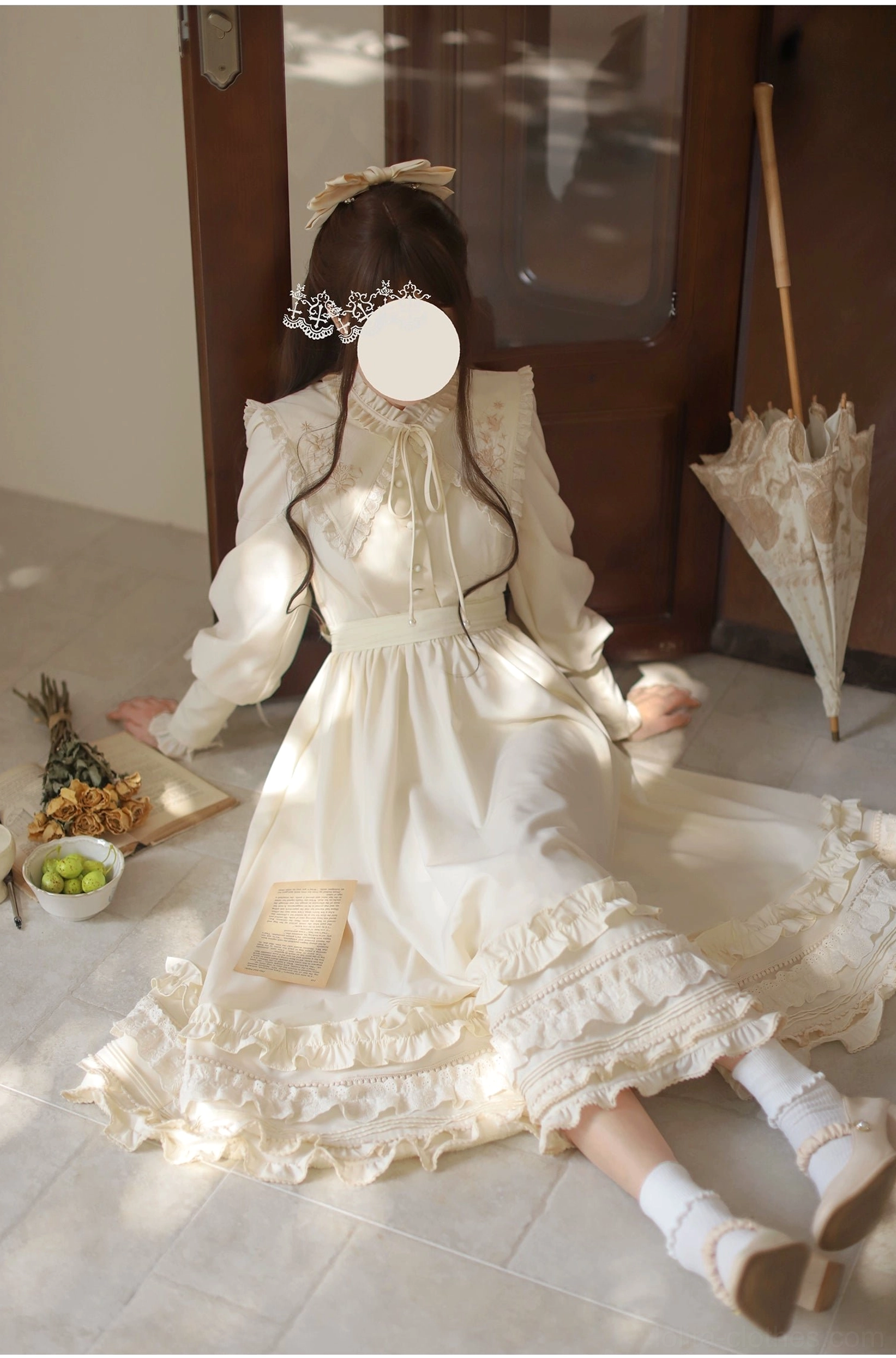 Full-body back view of apricot Lolita OP dress, trailing ruffled floor skirt, long sleeves, decorative hair bow accessory, seated pose with vintage décor styling