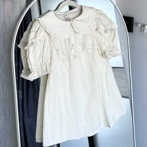 Apricot solid color sweet lolita short sleeve blouse full front mirror view showing ruffled peter pan collar layered ruffle puff sleeves vertical stripe fabric and a-line silhouette on model with arched mirror background