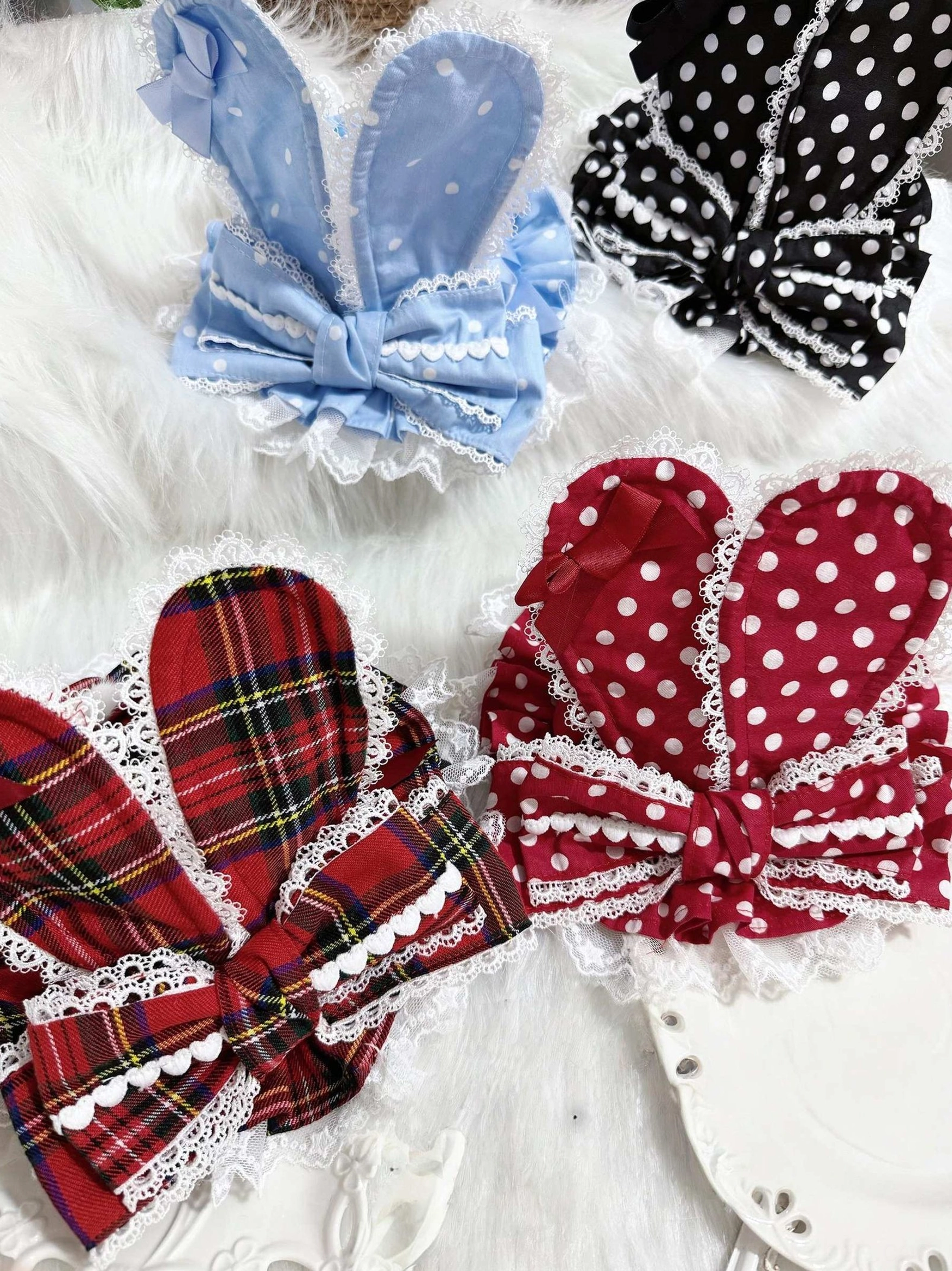 Assorted Lolita bunny ear hair bow clip styles collection including blue satin black polka dot red plaid and red polka dot with lace trim and bow details on white fuzzy fabric