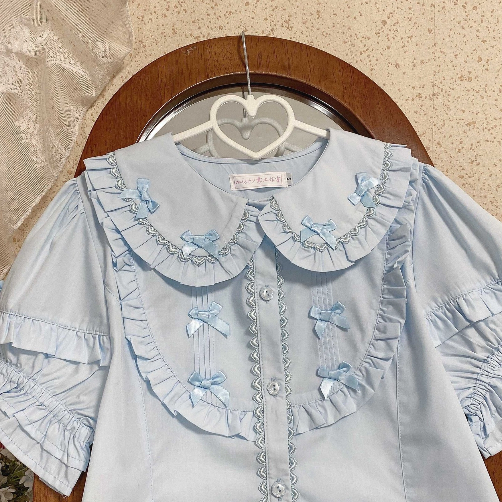 Baby blue lolita short sleeve blouse with matching blue satin bows on ruffled collar front button closure layered puff sleeves on heart hanger flat