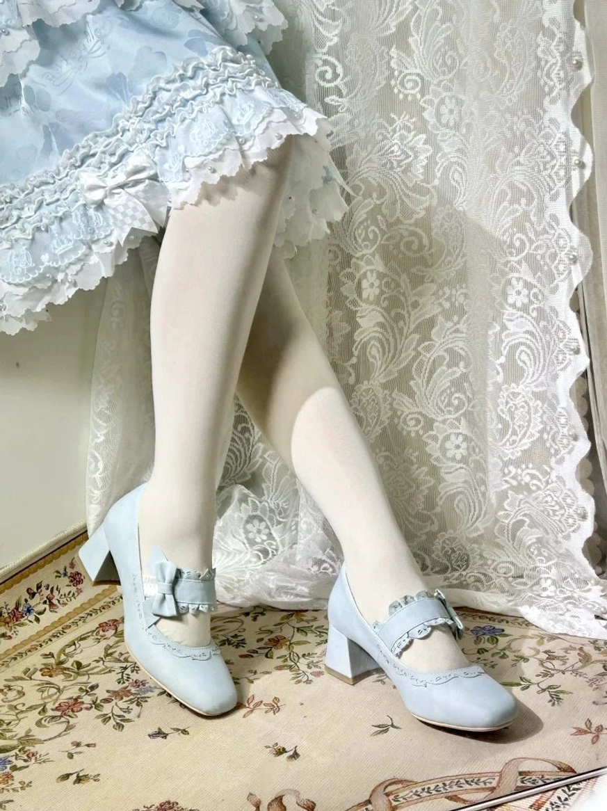 Baby blue lolita mary jane chunky heels with small decorative bow on elastic strap and delicate lace trim on vamp, low front view of on-foot wear, model wearing light blue ruffled skirt and white stockings