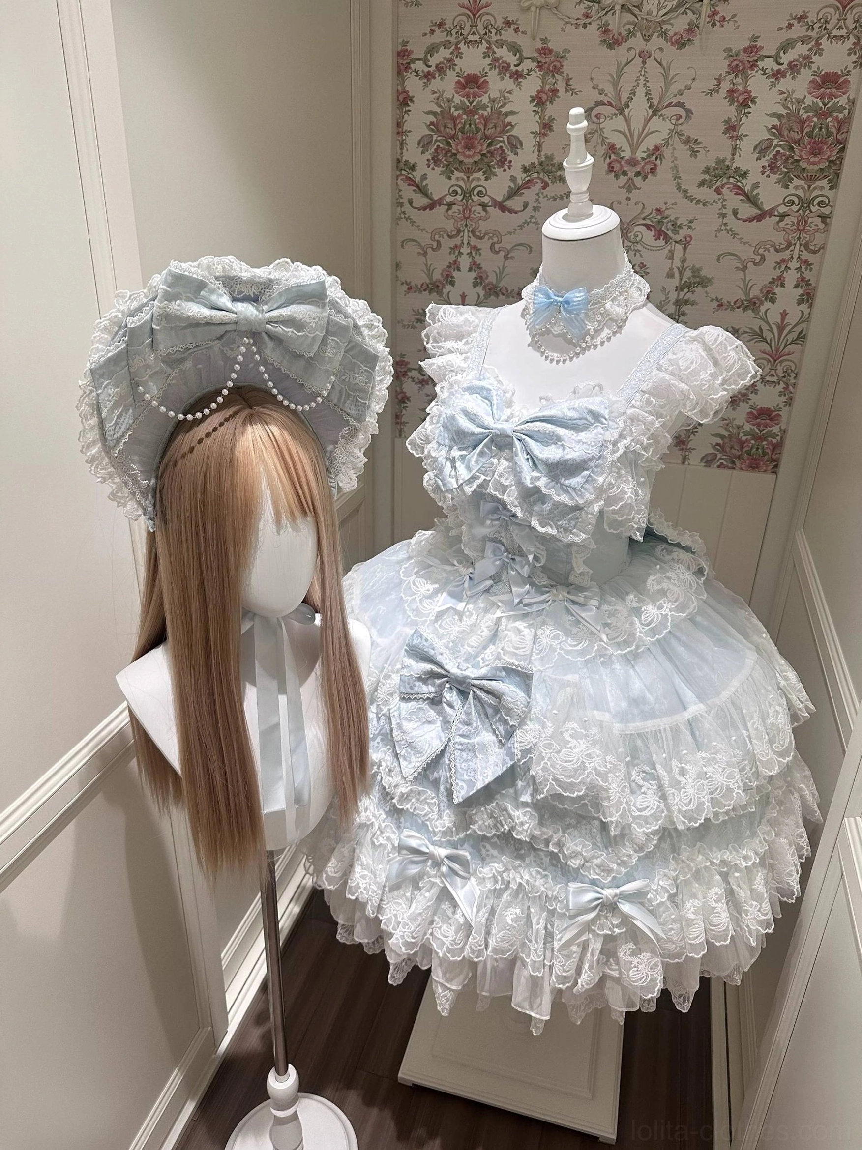 Baby blue Sakura Blossom Dream Sweet Lolita accessories collection featuring oversized blue BNT bonnet with pearl chain ornaments and layered lace trailing, matching blue satin choker necklace, full frontal view on dress mannequin with vintage showroom setting demonstrating Sweet Lolita aesthetic