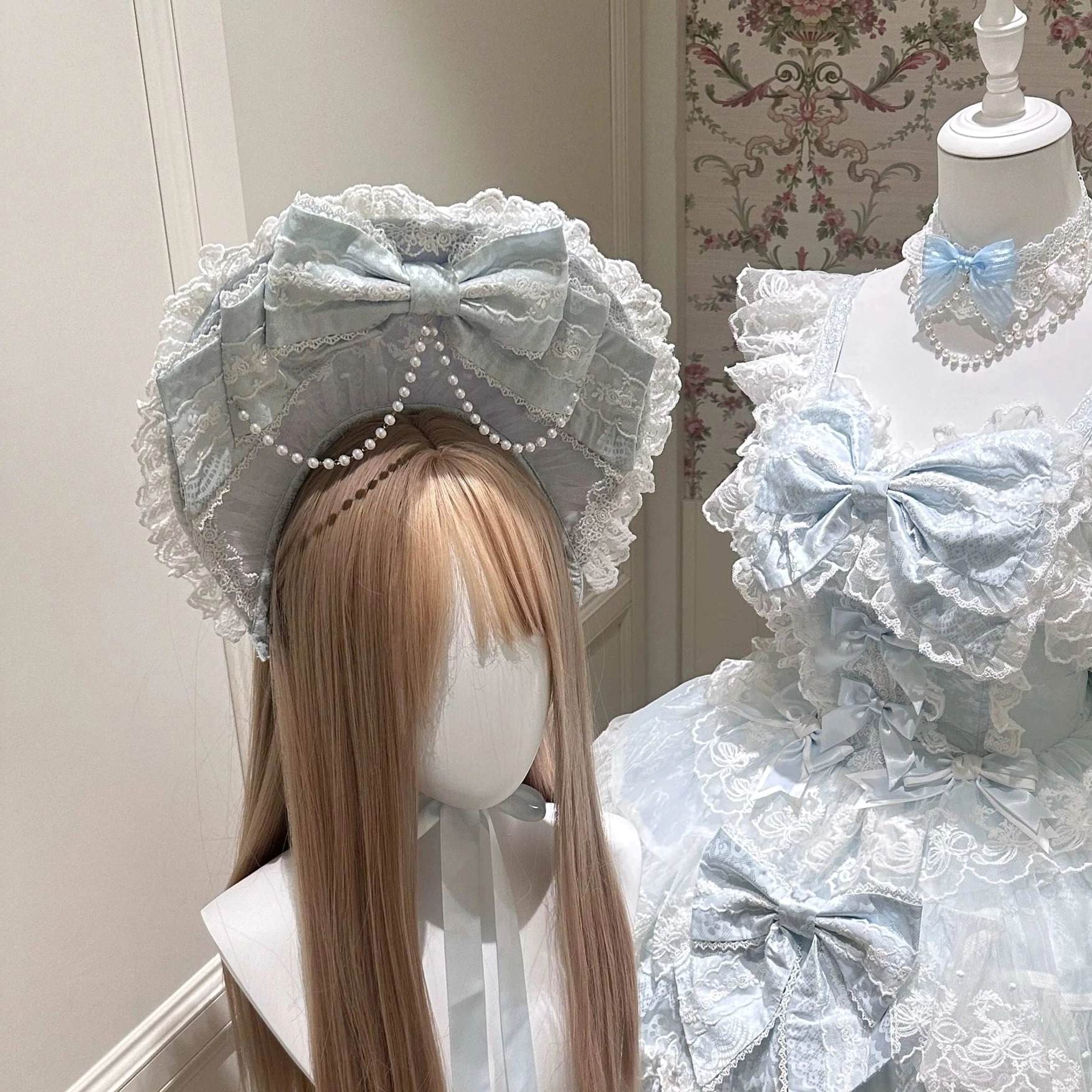 Front medium close-up of baby blue Sakura Blossom Dream Sweet Lolita complete accessory set showing pearl-decorated blue BNT bonnet with lace detailing, delicate blue choker necklace with faux pearl chains, layered lace ruffled neckline, multiple large decorative bows on bodice and skirt, and coordinating lace trim throughout