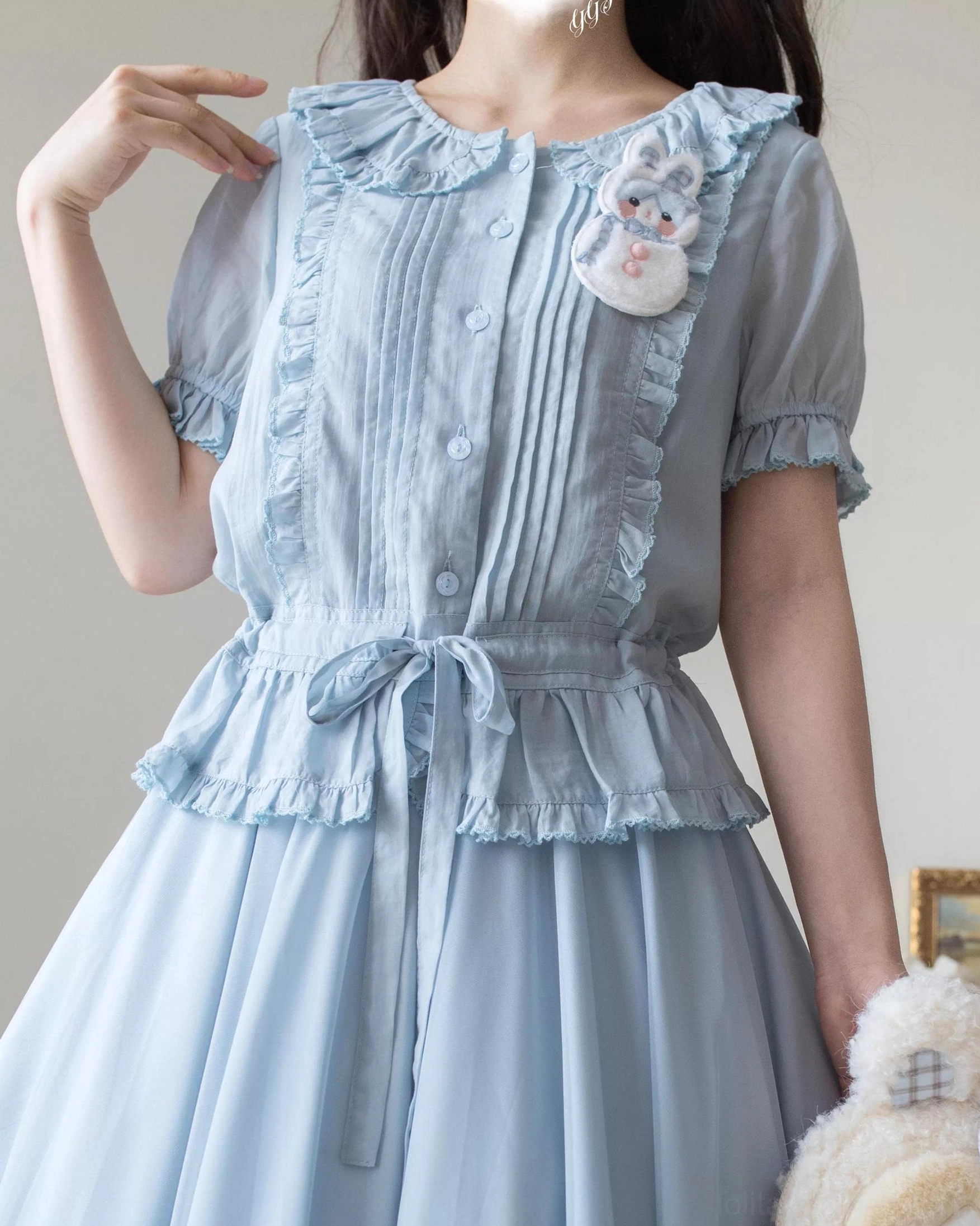 Baby blue Tencel semi-sheer sweet Lolita short-sleeve shirt three-quarter view showing Peter Pan collar, front lace trims, waist bow decoration, and ruffled cuffs