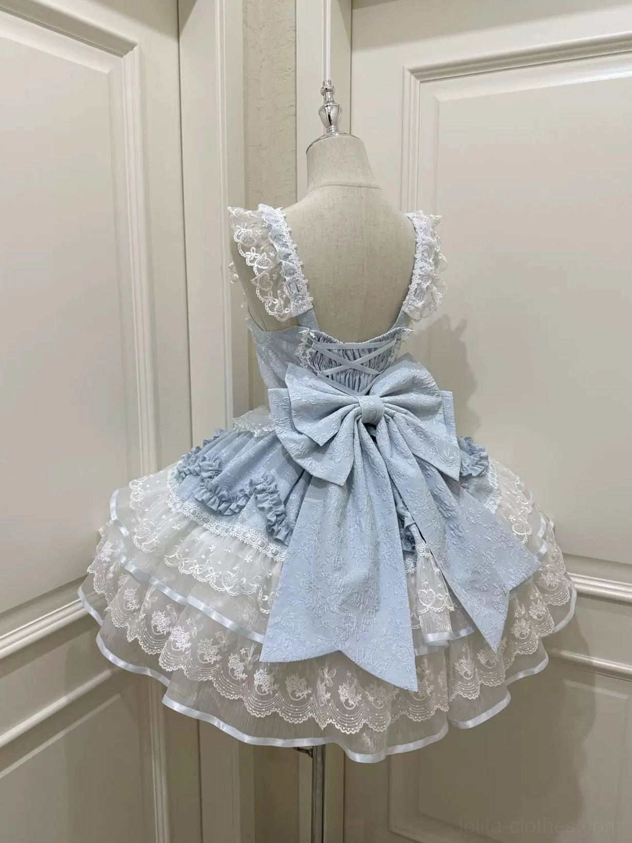 Rear display of baby blue sweet lolita JSK dress showing oversized blue satin back bow, ruffled shoulder straps, and lace-trimmed layered petal ruffled skirt