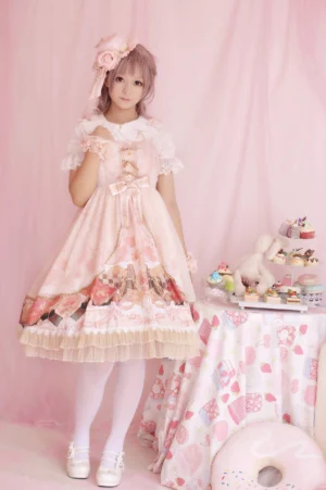 Baby pink summer lolita jumper skirt dress with lace ruffled sleeves and hemline, bowknot at bust, and floral pattern showcased on pink-haired model in tea party themed backdrop