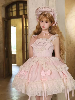 Baby pink sweet lolita jumper skirt half-body front view with cream lace trims pink bows and ribbon tassels worn with curly blonde hair pink lace bonnet vintage indoor room setting