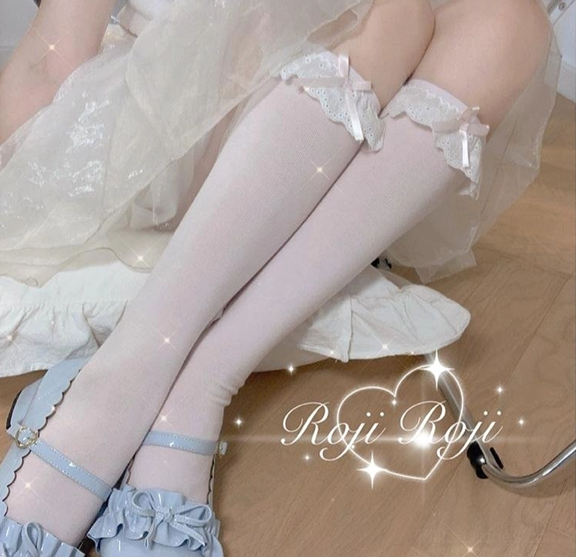 Baby pink lace-trimmed sweet lolita knee-high socks with tiny bow accents and soft knit fabric, close-up side view of crossed legs with light blue bow Mary Jane shoes on lace bedding