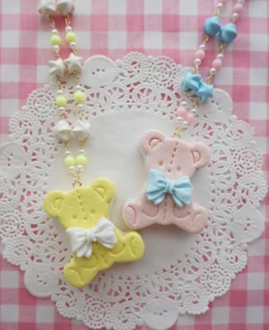 Yellow and light pink bear cookie clay necklace with cute bow decorations displayed on pink gingham background with white lace, pastel beaded chain detail