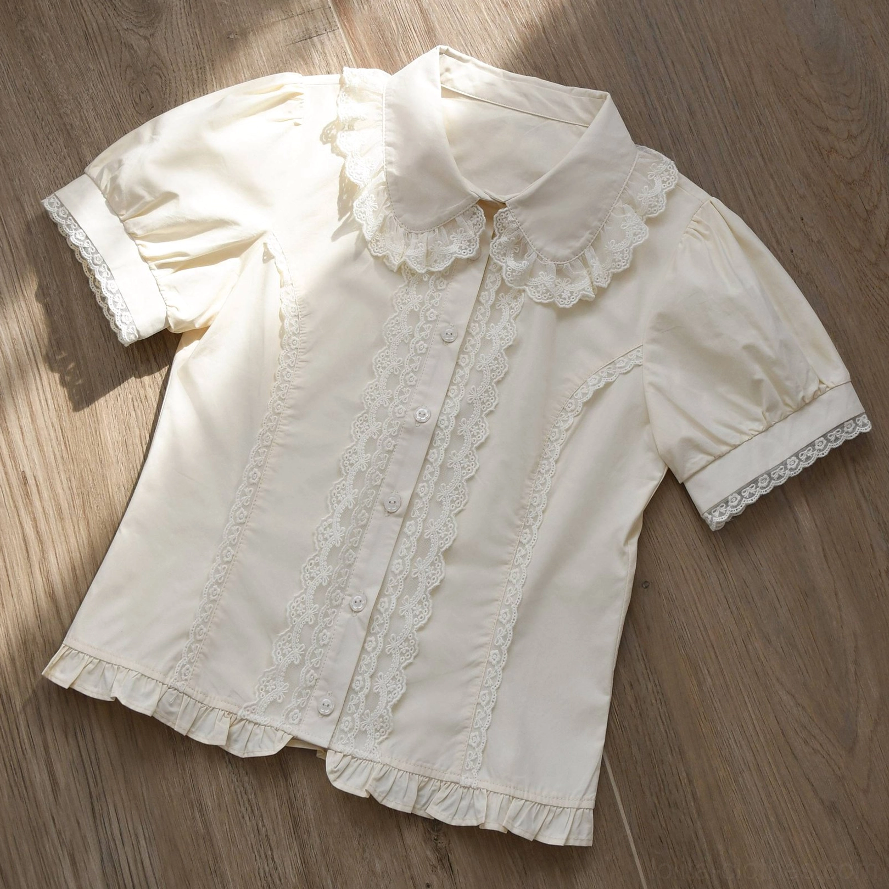 Cream beige vintage Lolita short-sleeve blouse with double-layer lace ruffled collar puff sleeves with lace cuffs and ruffled hem flat lay wooden background