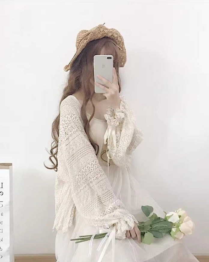 Front angle view of beige oversized lolita cardigan with crocheted hollow fabric and flowy open hem, model holding white rose bouquet