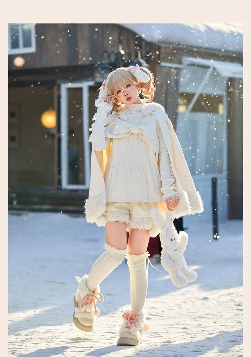 Beige rabbit ear hooded lolita cape with plush trim details and fluffy tail back accent paired with pom-pom decorated shorts displayed on model full-length front view