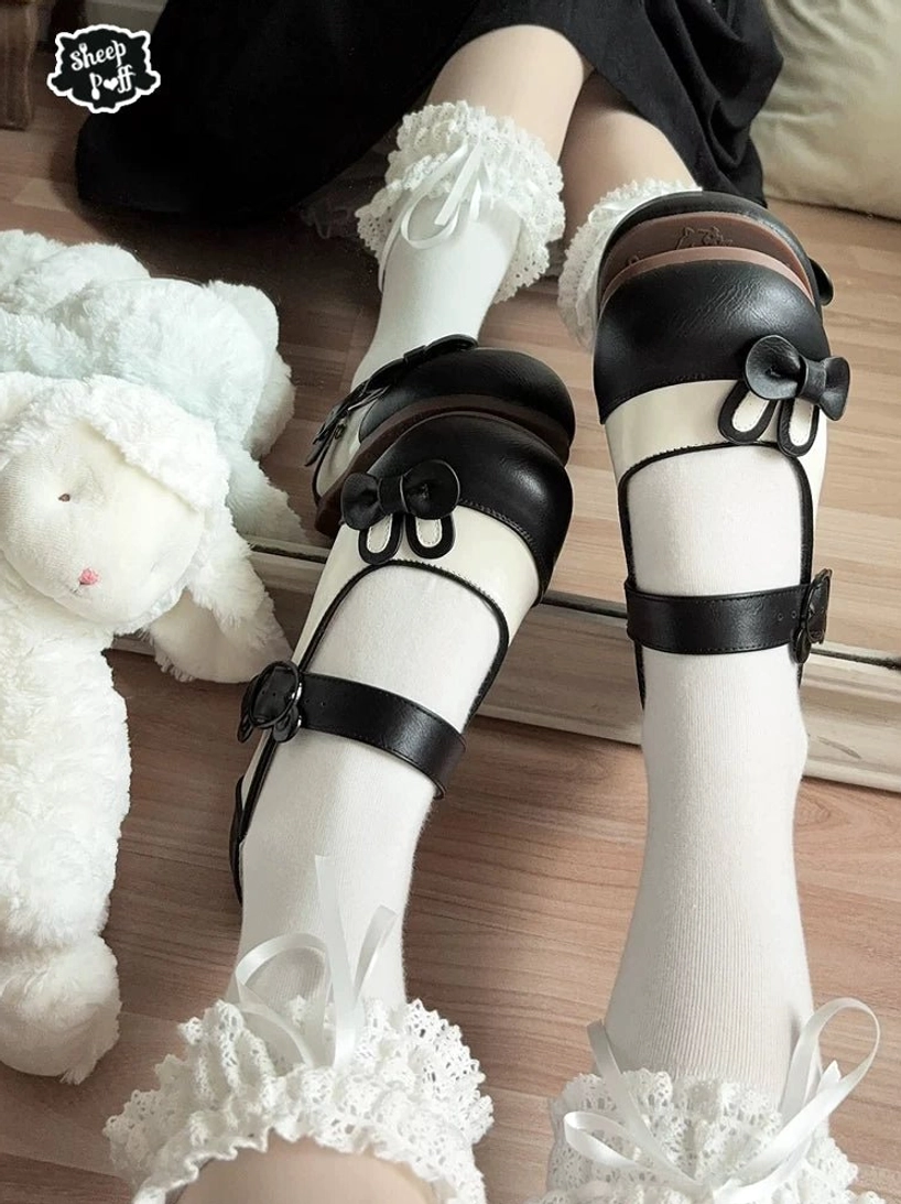 Black bunny bow lolita Mary Jane shoes worn with white ruffled socks surrounded by plush rabbit toys showing glossy finish and dual adjustable ankle straps