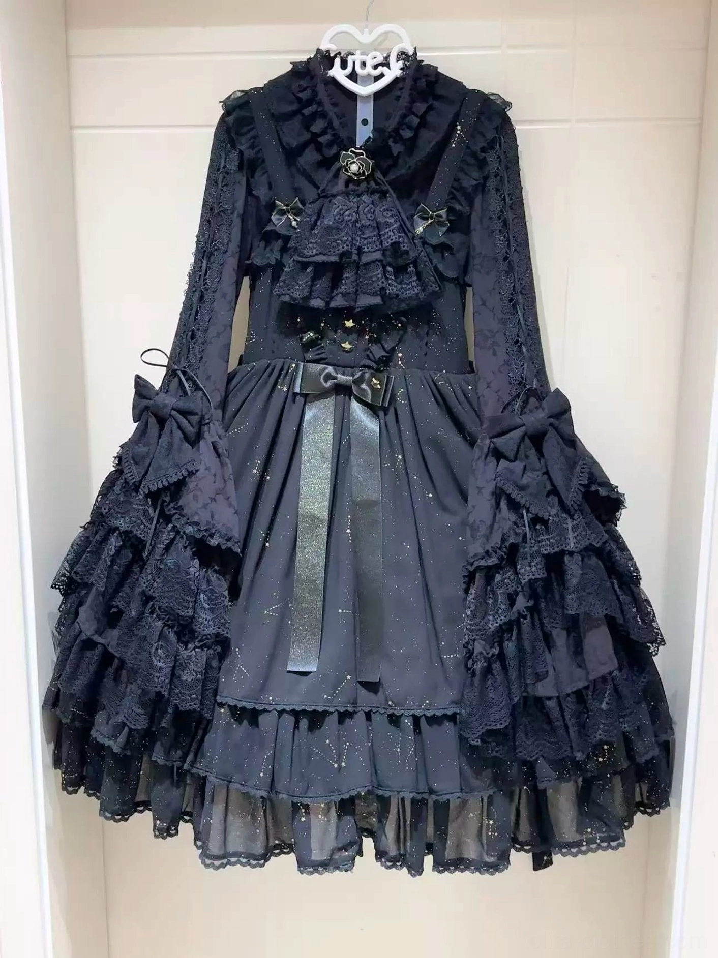 Black classic lolita blouse with layered ruffled lace jabot and bow details displayed on hanger with multi-tiered ruffle collar design visible