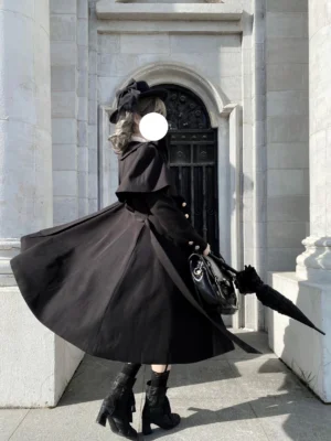 Back view of elegant black Lolita long coat with full flared A-line hem and fitted waist, showcasing twill fabric matte finish and dramatic proportions in outdoor architectural setting