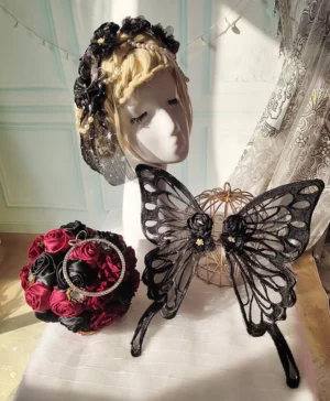 Black embroidered lace butterfly hair clip with sheer mesh wings and fabric rose details displayed on vintage mannequin head with red bridal bouquet in overhead flat lay view