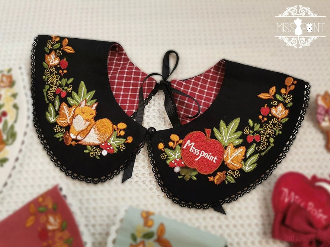 Black embroidered lolita faux collar overhead close-up flat lay light fabric backdrop red plaid inner lining fox floral embroidery apple shaped tag lace trim