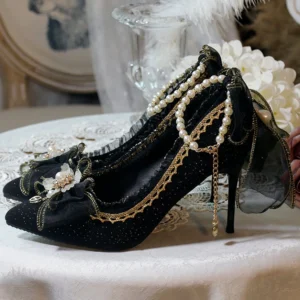 Pure black glitter lolita high heels with pointed stiletto heel, gold lace trim, pearl strings, large fabric bow and flower ornaments shown in side top-down view on lace tablecloth