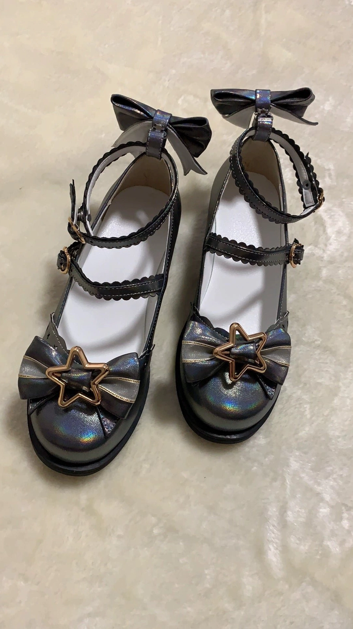 Black sweet lolita shoes with glitter effect under sunlight showing star gold hardware front decorative bow double ruffled ankle straps and heel bow accent detail