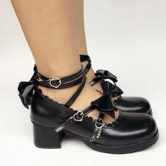 Side flat lay of black glossy sweet Lolita Mary Jane shoe featuring dual crisscross straps with heart-shaped buckles, bow decorations, and scalloped collar