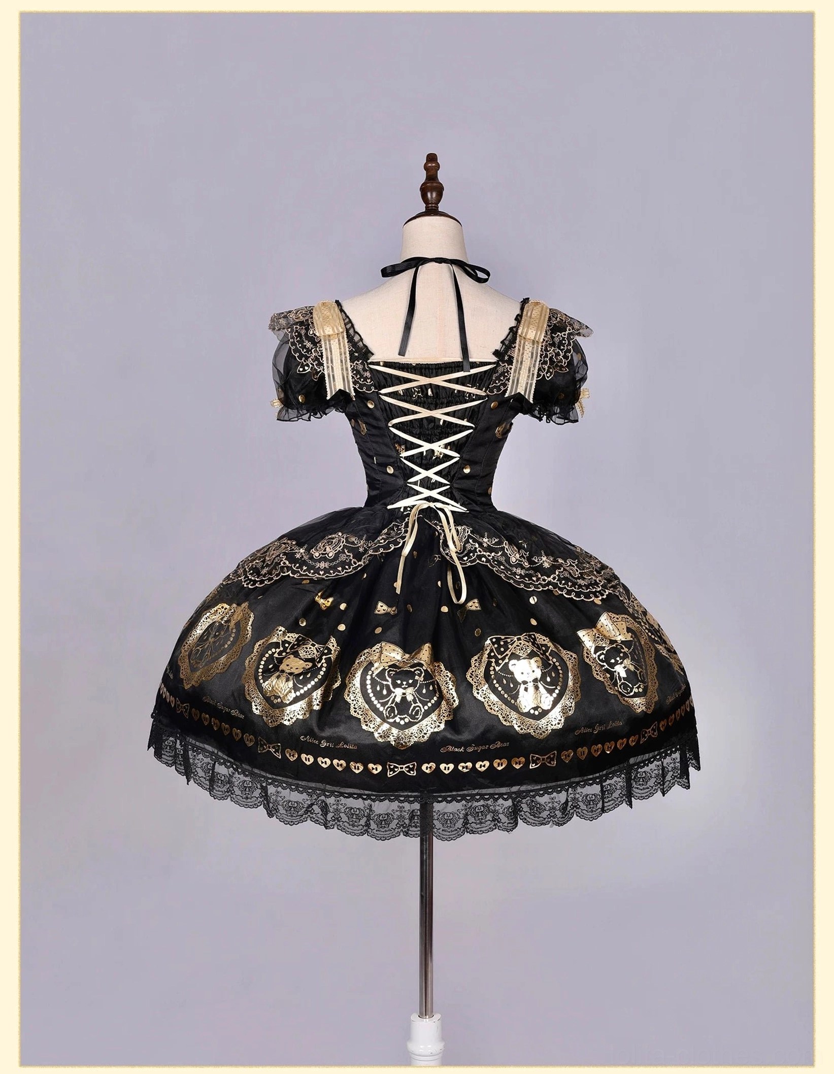 Back view of black and gold bear print lolita dress on dress form showing lace-up corset back, ruffled off-shoulder sleeves, black lace skirt trim and gold bear print details