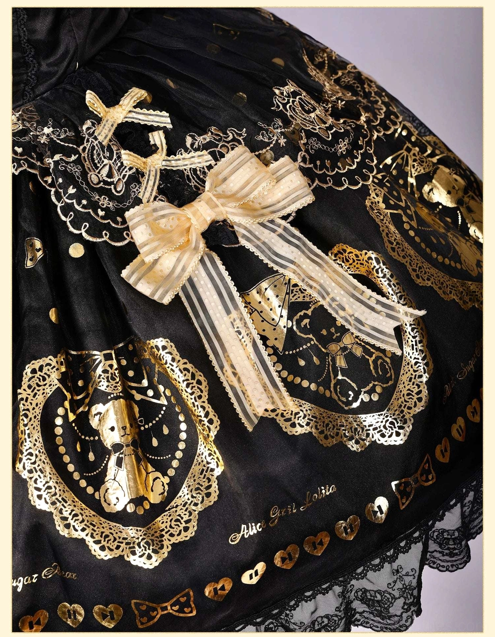 Close-up side view of lolita dress skirt showing vintage gold teddy bear frame prints, delicate lace skirt trim, large gold satin bow with ribbon streamers, mini gold heart prints and embroidery