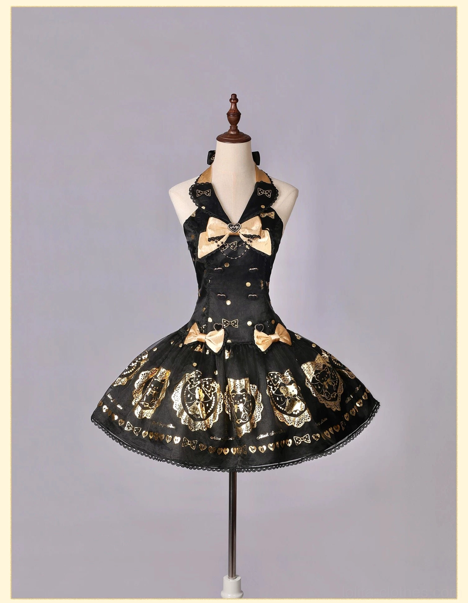 Halter-neck black and gold bear print lolita dress on dress form with large gold bow, flared short skirt with teddy bear motif patterns, against neutral gray studio backdrop