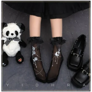 Black sheer Gothic Lolita ankle socks with ruffled lace cuff and floral bird printed patterns paired with panda plush toy and black leather loafers overhead view