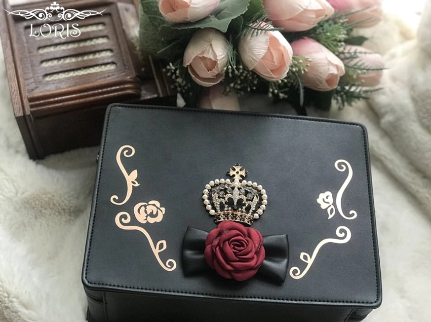 single black gothic lolita crown handbag front flat lay view jeweled crown ornament red rose black bow golden scroll motifs leather handle white fuzzy backdrop wooden decor