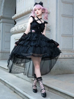 Black Gothic Classic Lolita high-low hem JSK dress with rose details, front three-quarter view worn by model with pink twin curly buns, lace socks, and coordinating accessories in European vintage stone arch setting