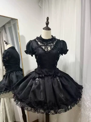 Black Gothic Lolita OP dress front view on mannequin featuring puffed short sleeves, sheer lace yoke neckline with satin fabric, lace hemmed mini skirt, decorative waist bows and cross trims, captured against sheer white curtain backdrop