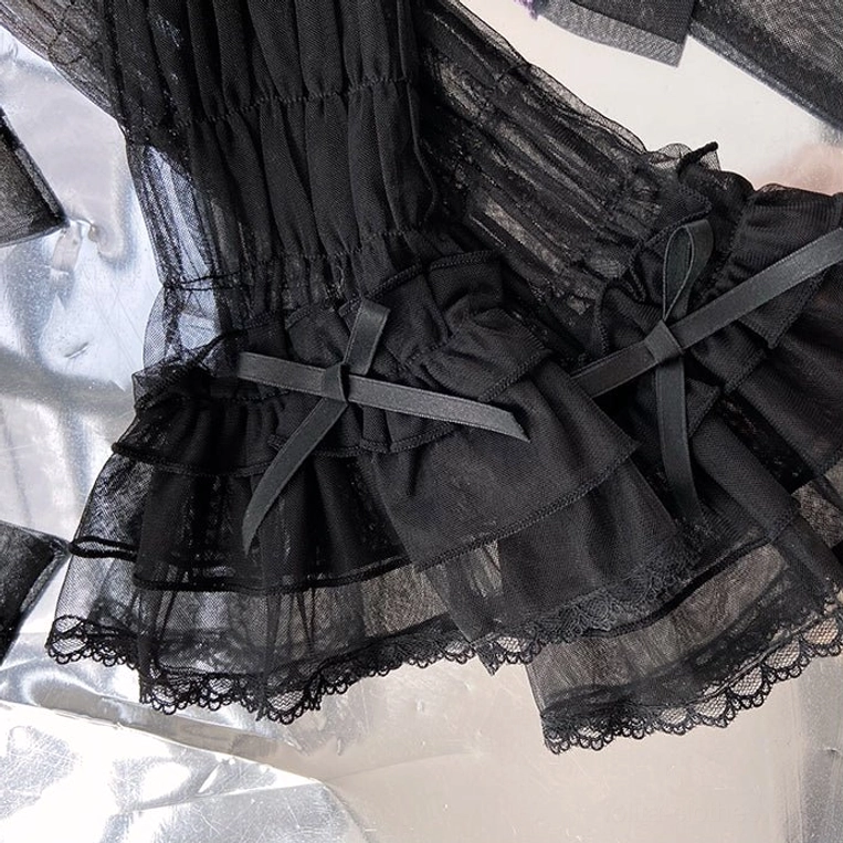 Close-up of black Gothic Lolita arm cuffs with tiered ruffled mesh, black satin ribbon bows and lace bottom trim on silver reflective fabric background