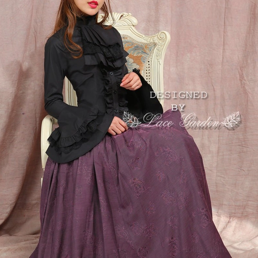 Black gothic lolita ruffled blouse seated front view on vintage chair, ruffled jabot flared trumpet sleeves front button design on female model