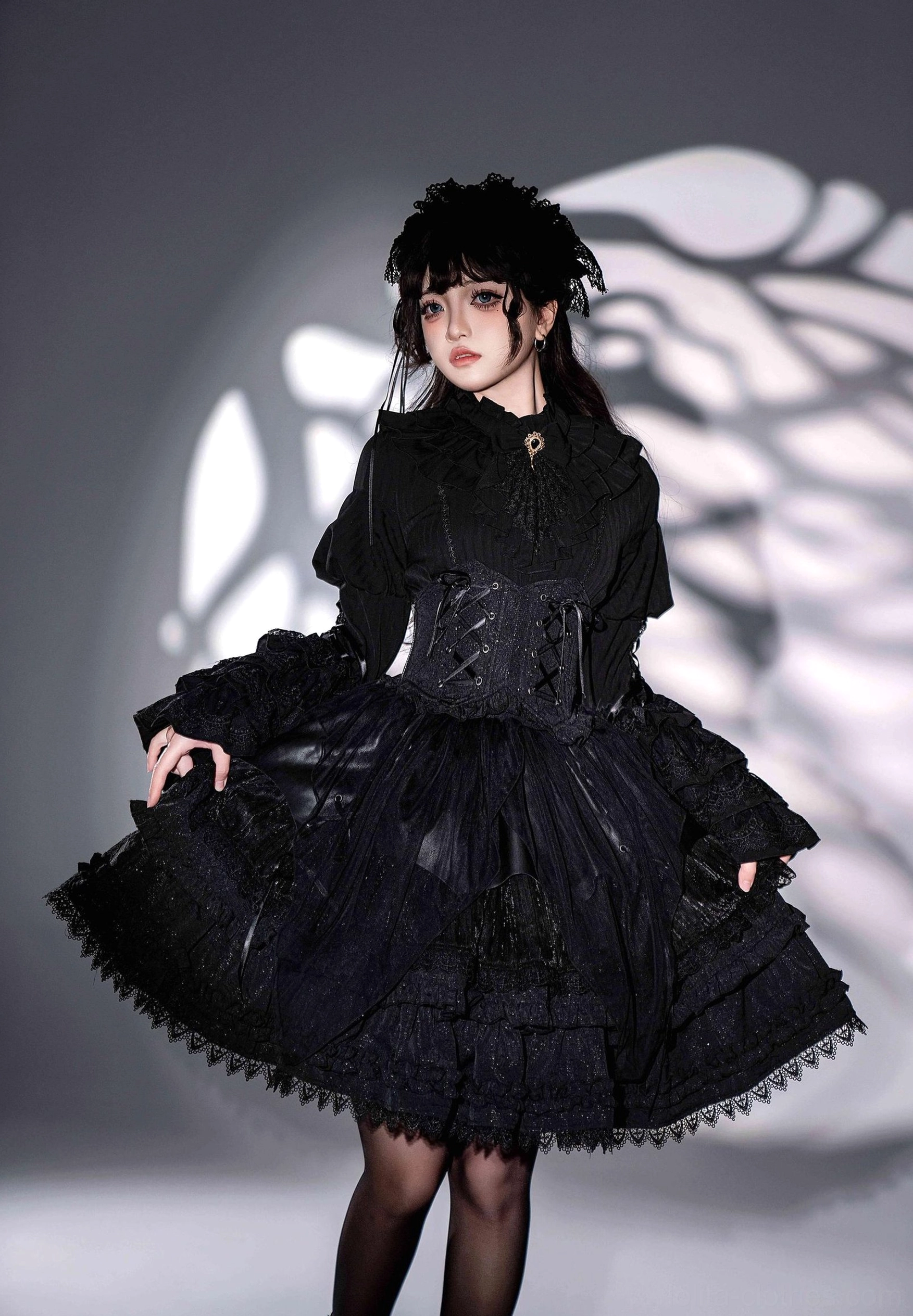 Single model wearing black gothic lolita corset dress with wide bell sleeves lifting skirt hem to display layered ruffle construction and lace trimmed hem details