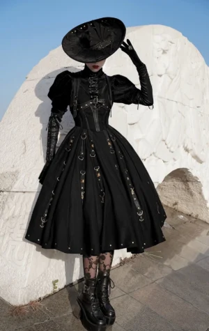 Full-body front view of black gothic pirate lolita jumper skirt with mutton sleeves blouse set, model wearing wide-brim gothic hat and lace stockings with combat boots on outdoor stone sculpture backdrop
