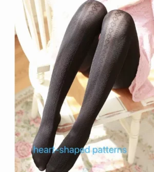 Black heart-shaped jacquard patterned lolita pantyhose front view bent legs white chair pink fabric