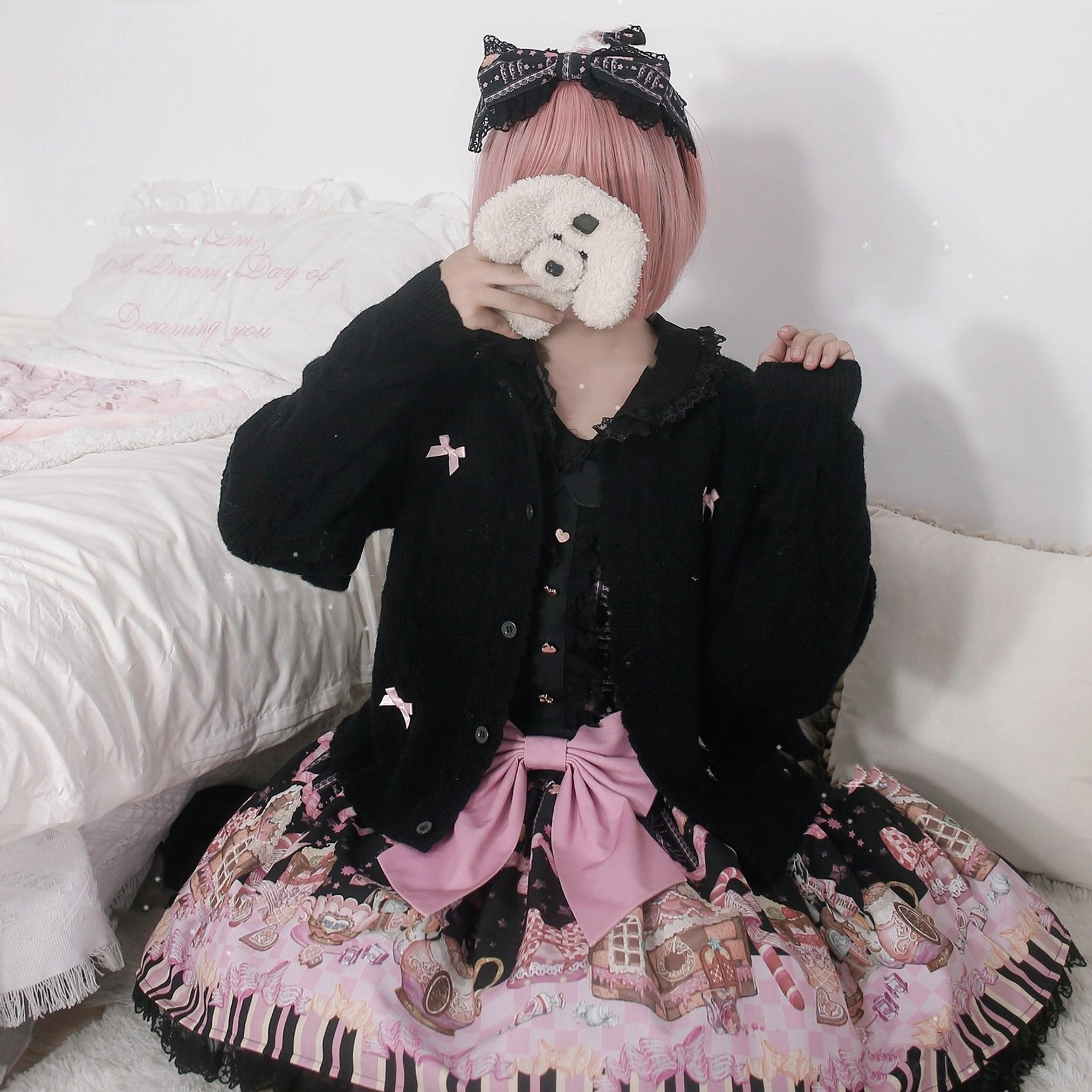 Black hollow out long sleeve Lolita cardigan with small bow embellishments and front button closure paired with printed Lolita skirt, model with pink short hair sitting